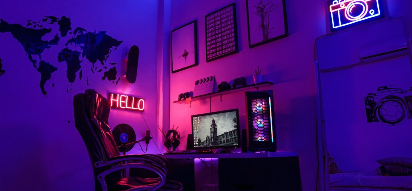 A gaming workspace with a computer, neon signs, and wall art in purple light