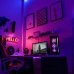 A gaming workspace with a computer, neon signs, and wall art in purple light