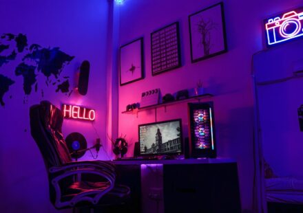 A gaming workspace with a computer, neon signs, and wall art in purple light