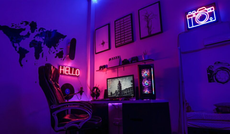 A gaming workspace with a computer, neon signs, and wall art in purple light